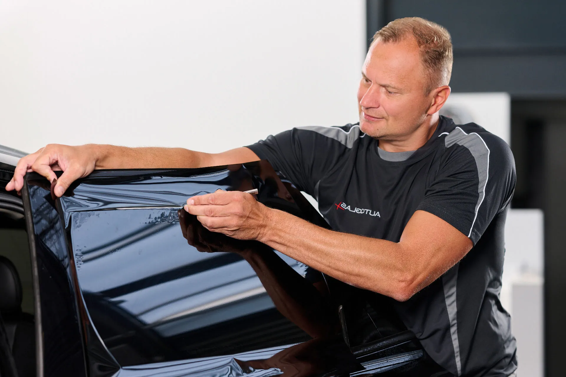 Ein Mann bringt eine Tönungsfolie an einer Autoscheibe an und streicht sie mit der Hand glatt.