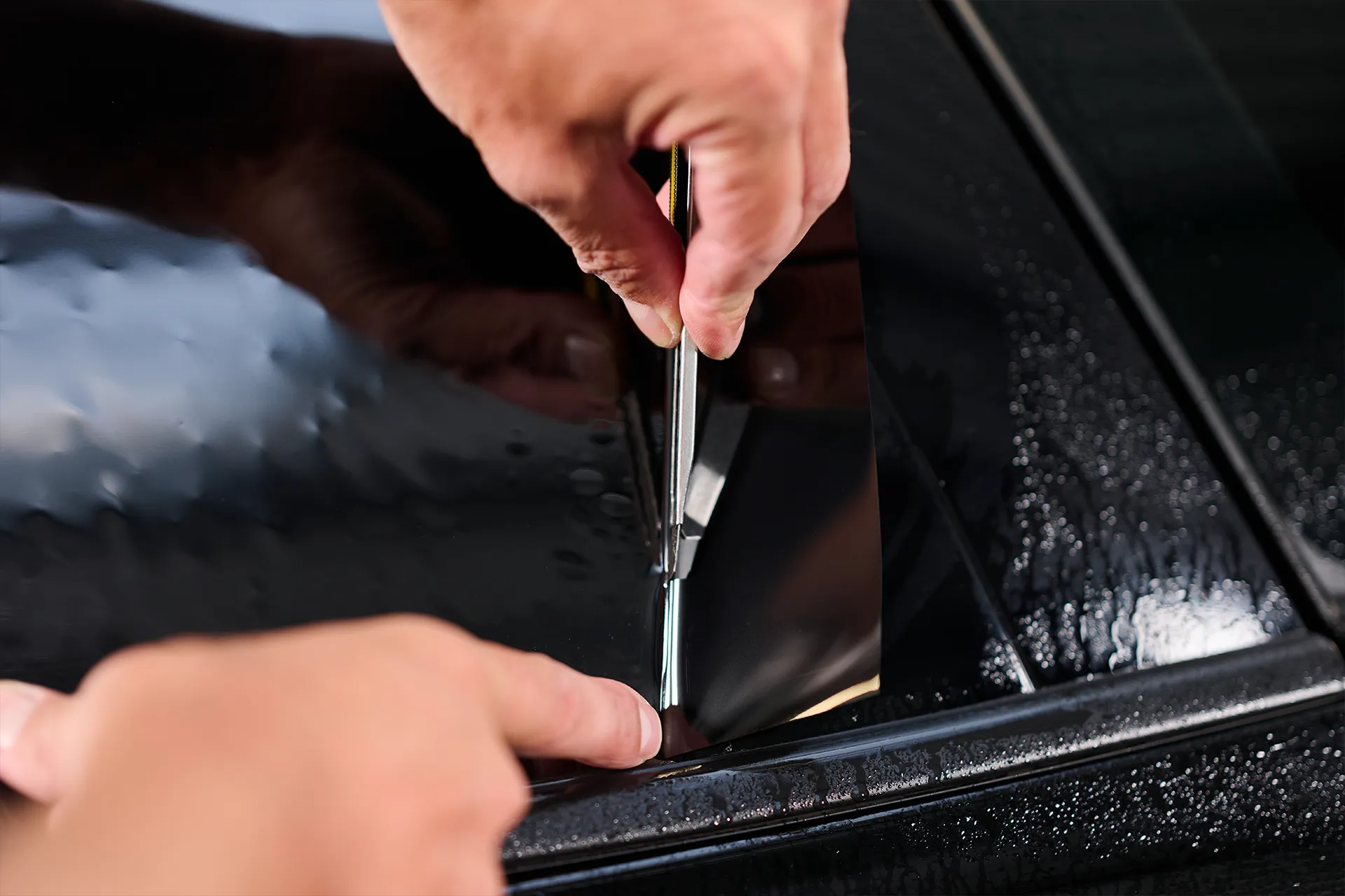 Eine Person schneidet mit einem Cuttermesser die Scheibentönungsfolie an einer Autoscheibe zurecht.