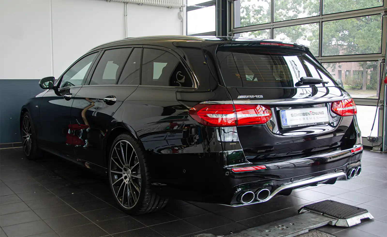 Ein schwarzer Mercedes-AMG-Kombi steht in einem Innenraum auf einem Fliesenboden, während durch große Fenster Tageslicht hereinfällt.